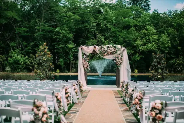 An outdoor wedding aisle leading to a flowered arbor beside the Bayou Haven pond
